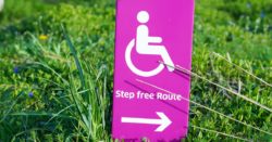 A white on pink sign with a pictogram of a wheelchair and the arrow pointing to a wheelchair accessible route. Text above the arrow says "Step free Route"