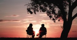 Silhouette of two people sitting on the chairs near a tree at the sunset