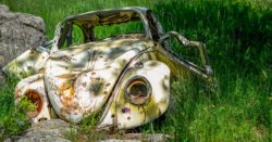 Old rusty wrecked white Volkswagen Beetle coupe on grass