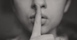A woman holding finger to the lips in a shoosh gesture
