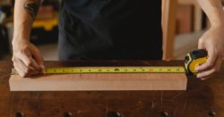 A photo of masculine hands measuring a block of wood with a tape measure.